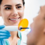 selective focus of female dentist making bleaching procedure to african american patient